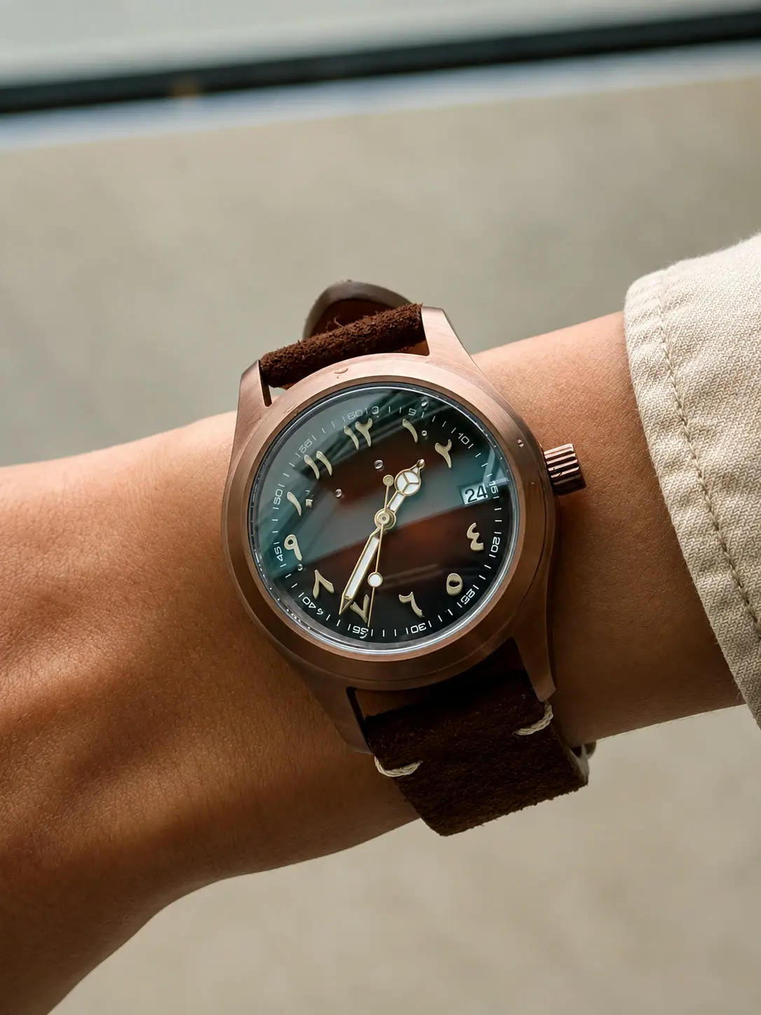 Bronze field build with a green fume dial and Arabic numerals on a brown suede strap, worn on a wrist.