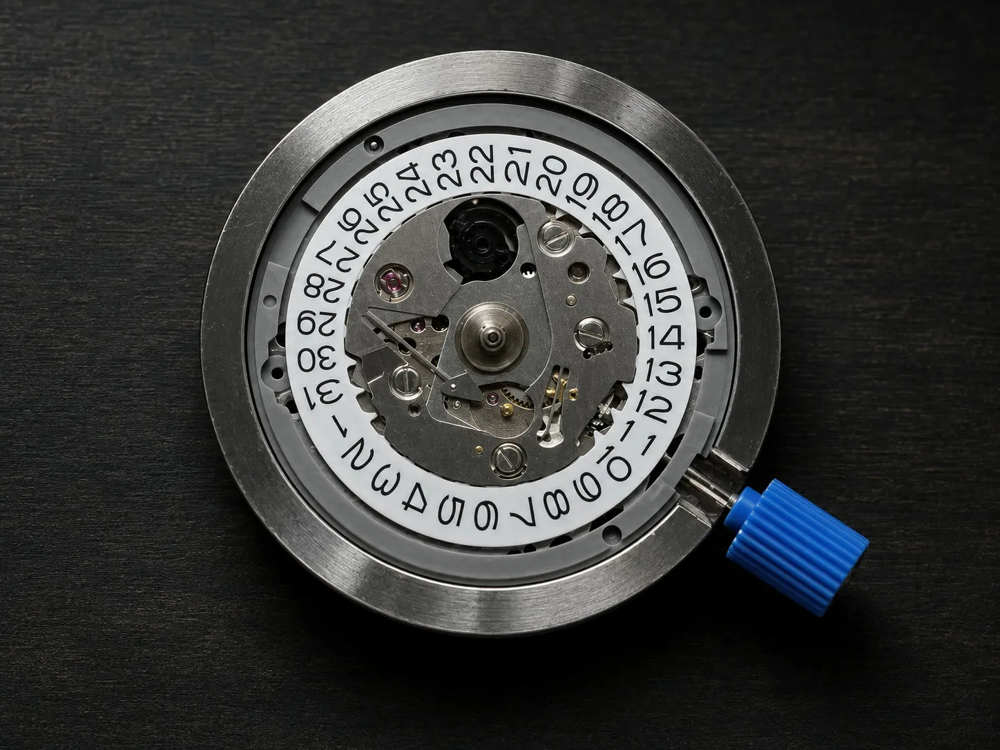 Dial side of a Seiko NH35 movement, showing the white date wheel and the blue plastic stem protector, resting on a dark surface.