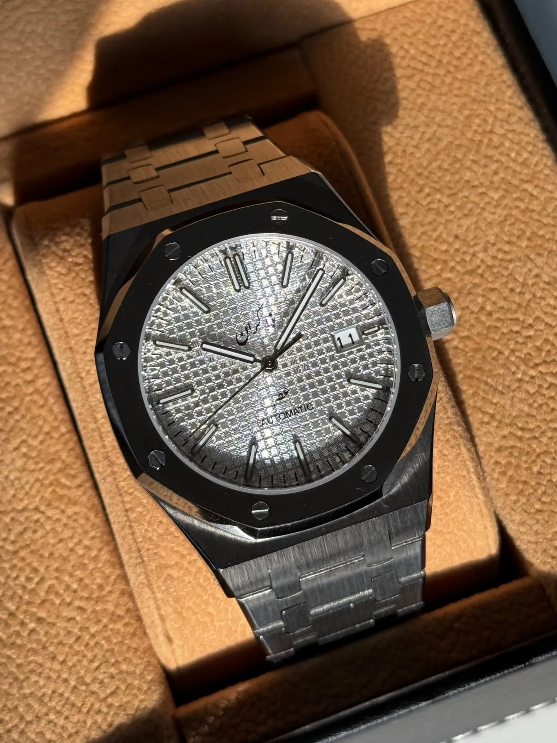 Octagonal bezel build with exposed screws and a silver textured dial on an integrated bracelet.