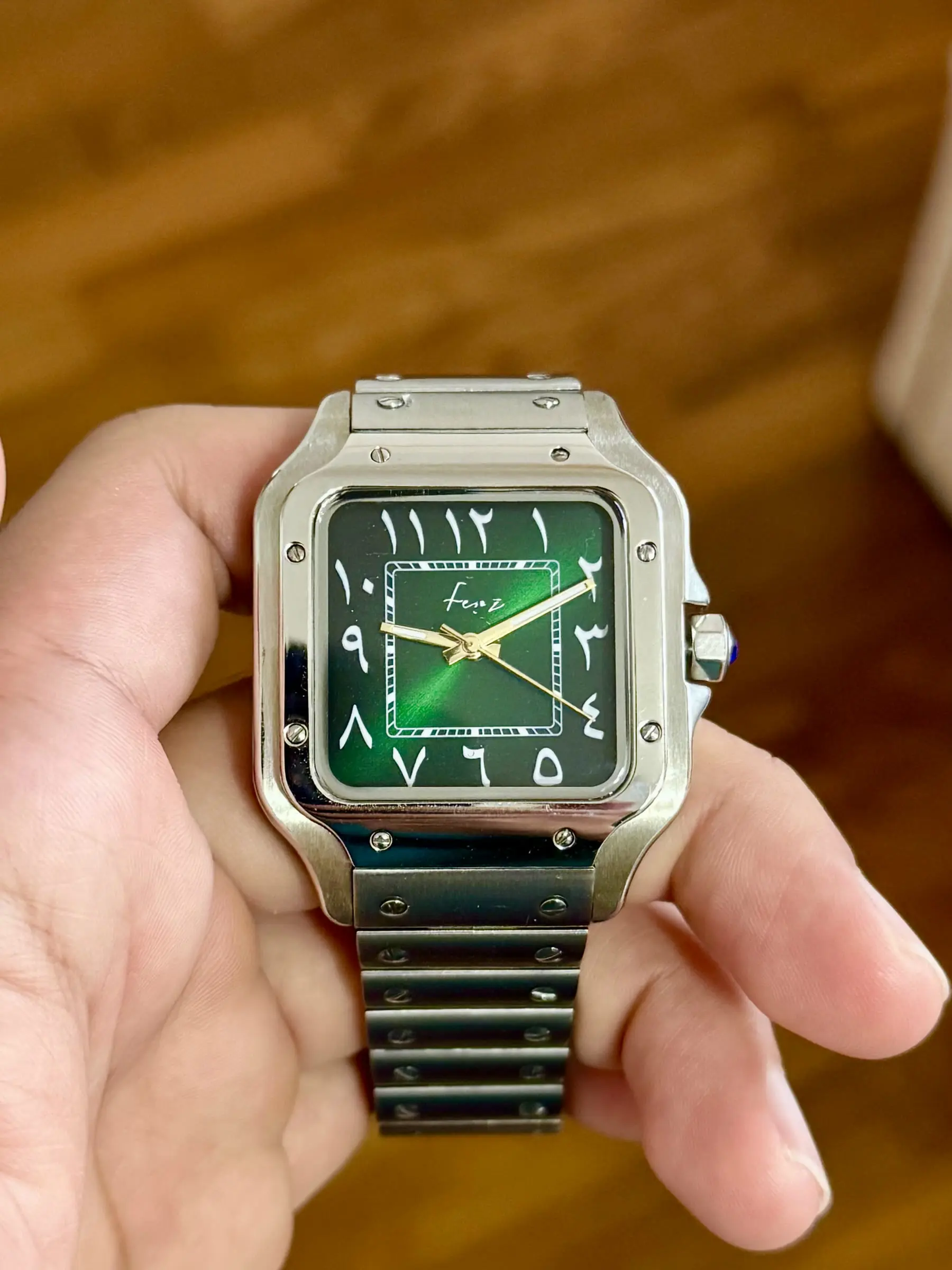 Square cased build with a green dial and Arabic numerals on an integrated bracelet.